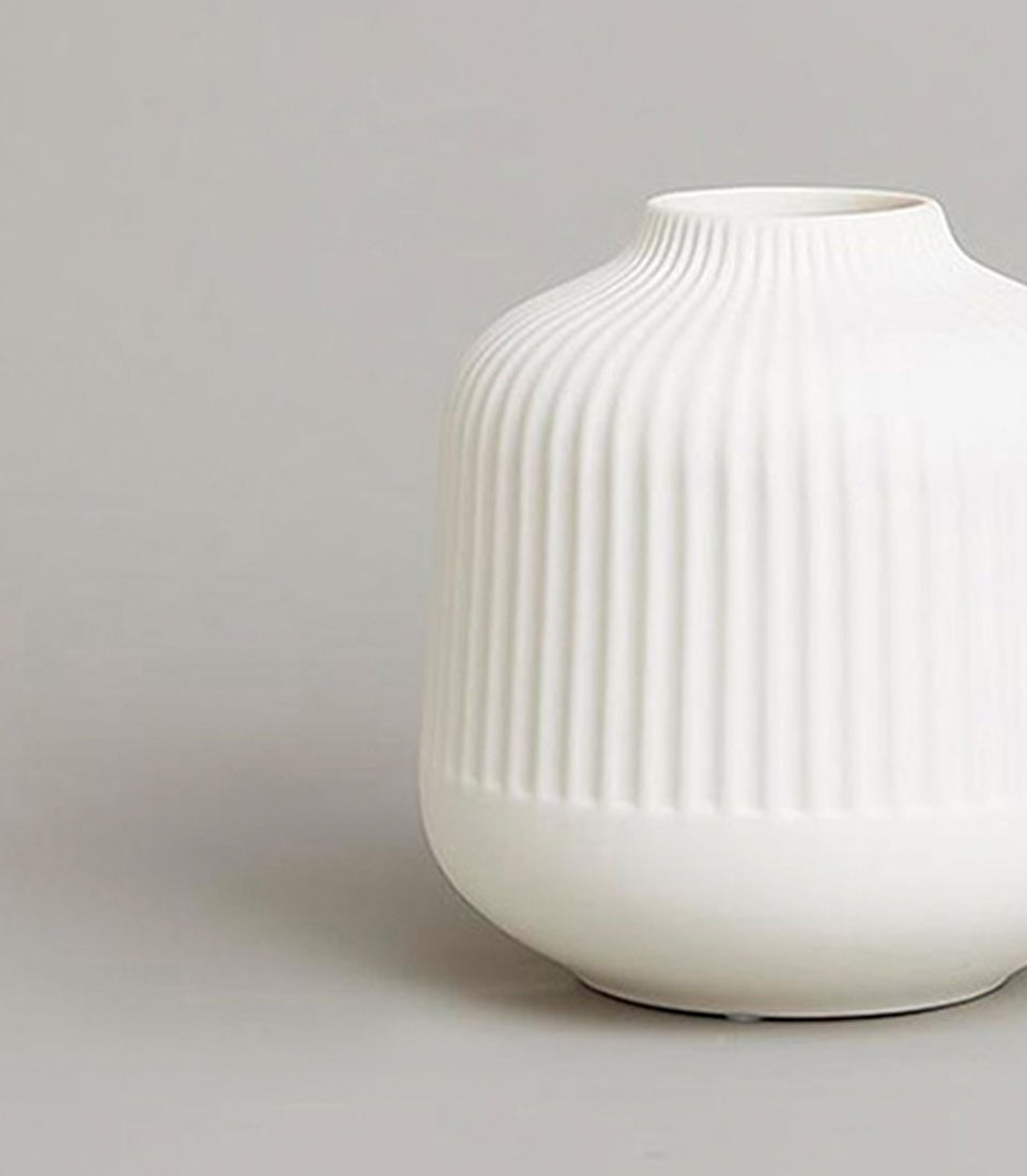 Elegant small white ceramic vase with vertical grooves, close-up view.