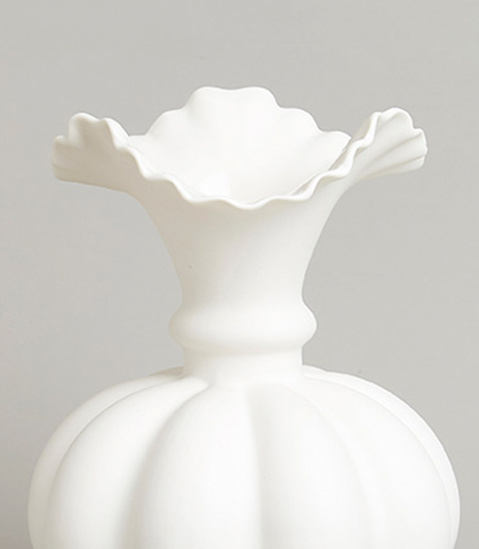 Close-up of white ceramic vase with scalloped top and rounded base.