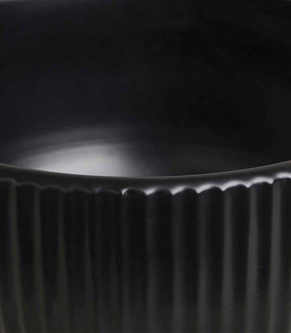 Pair of modern black ceramic planters with ribbed texture and cylindrical bases, in different sizes, on a light grey background