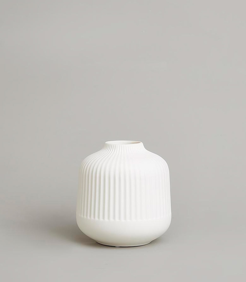Minimalist white ceramic vase with a ribbed texture and rounded shape, placed on a light grey background