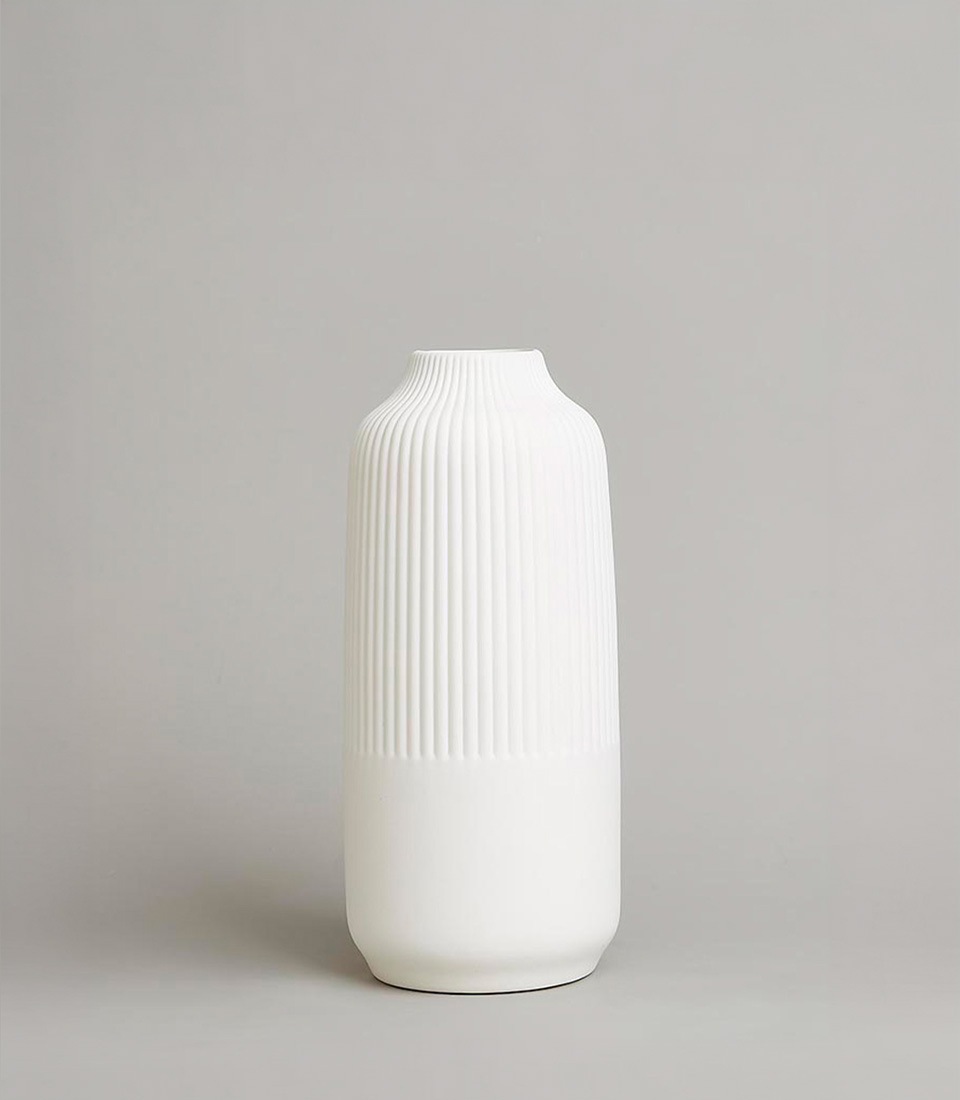 Minimalist tall white ceramic vase with ribbed texture and smooth finish, featuring a sleek cylindrical shape, on a light grey background.