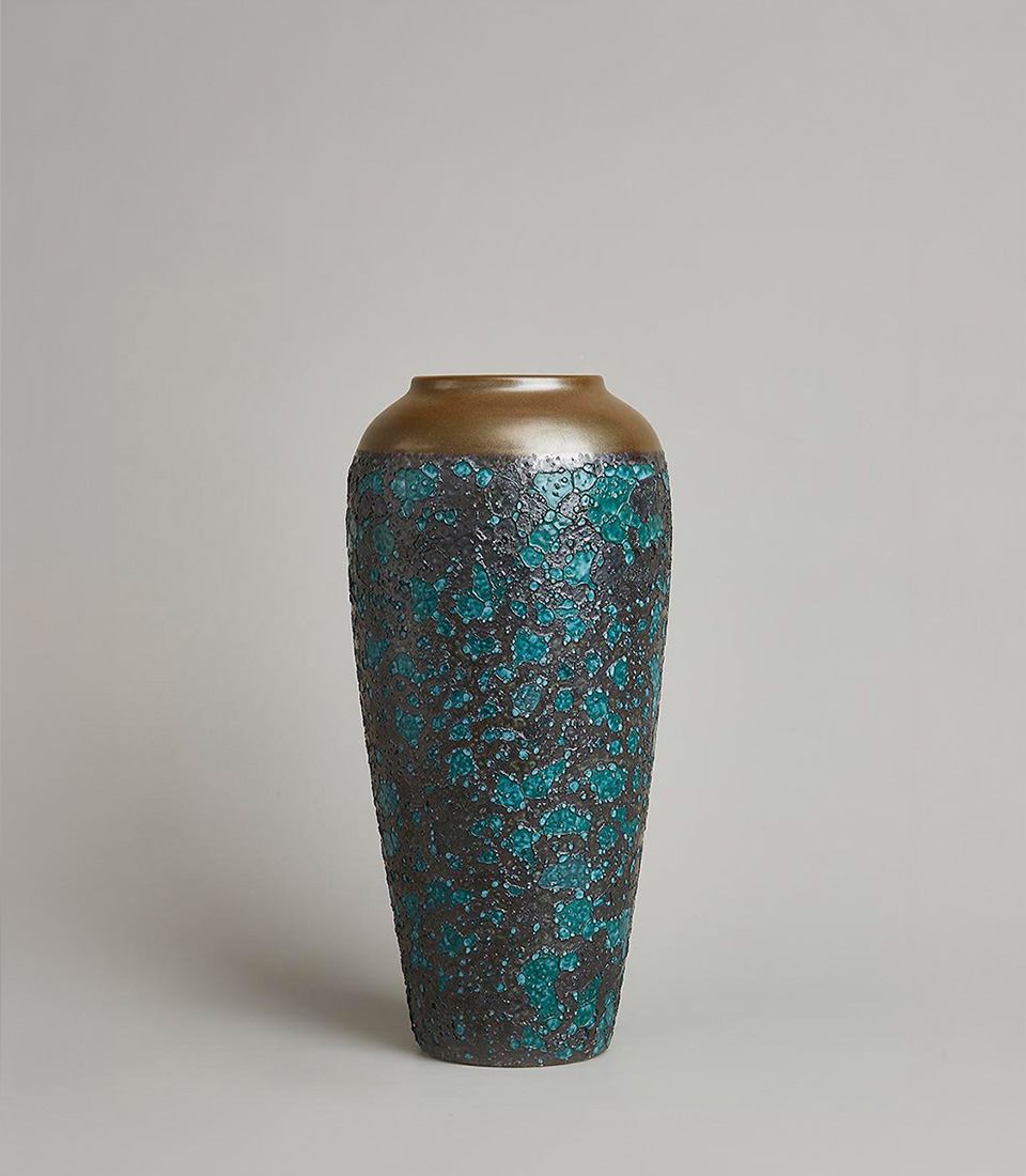 Large ceramic vase with a textured surface, featuring a blend of turquoise and black mosaic-like pattern, and a metallic bronze top rim, on a light grey background.