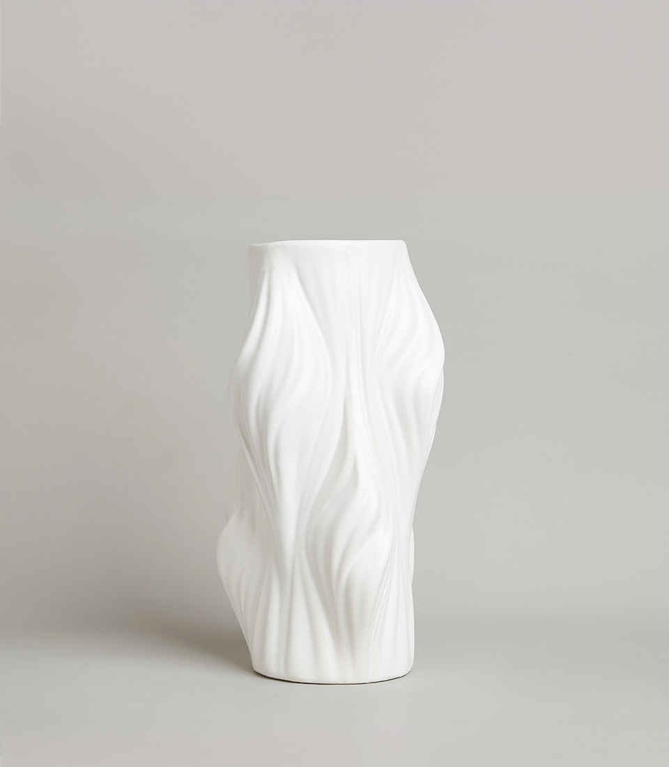 Contemporary white ceramic vase with an organic, flowing wave-like texture and sculptural form, placed on a light grey background