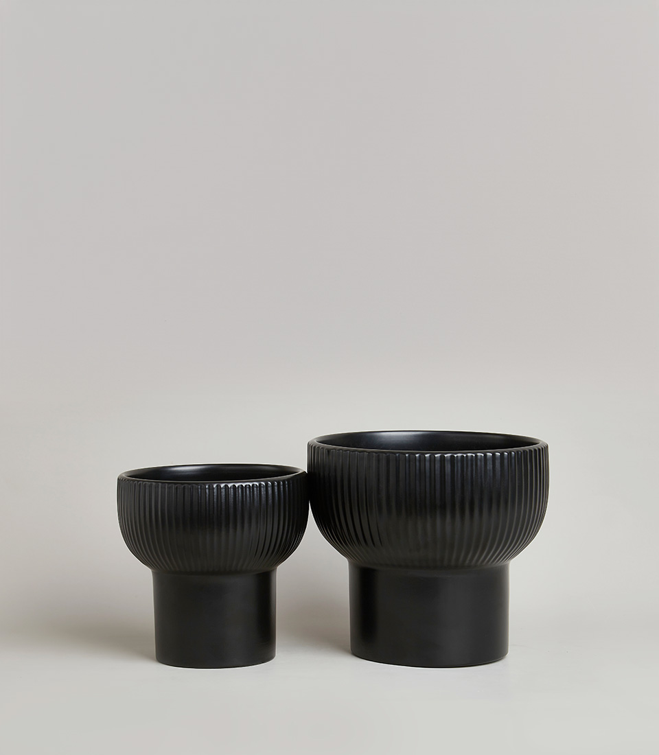 Pair of modern black ceramic planters with ribbed texture and cylindrical bases, in different sizes, on a light grey background