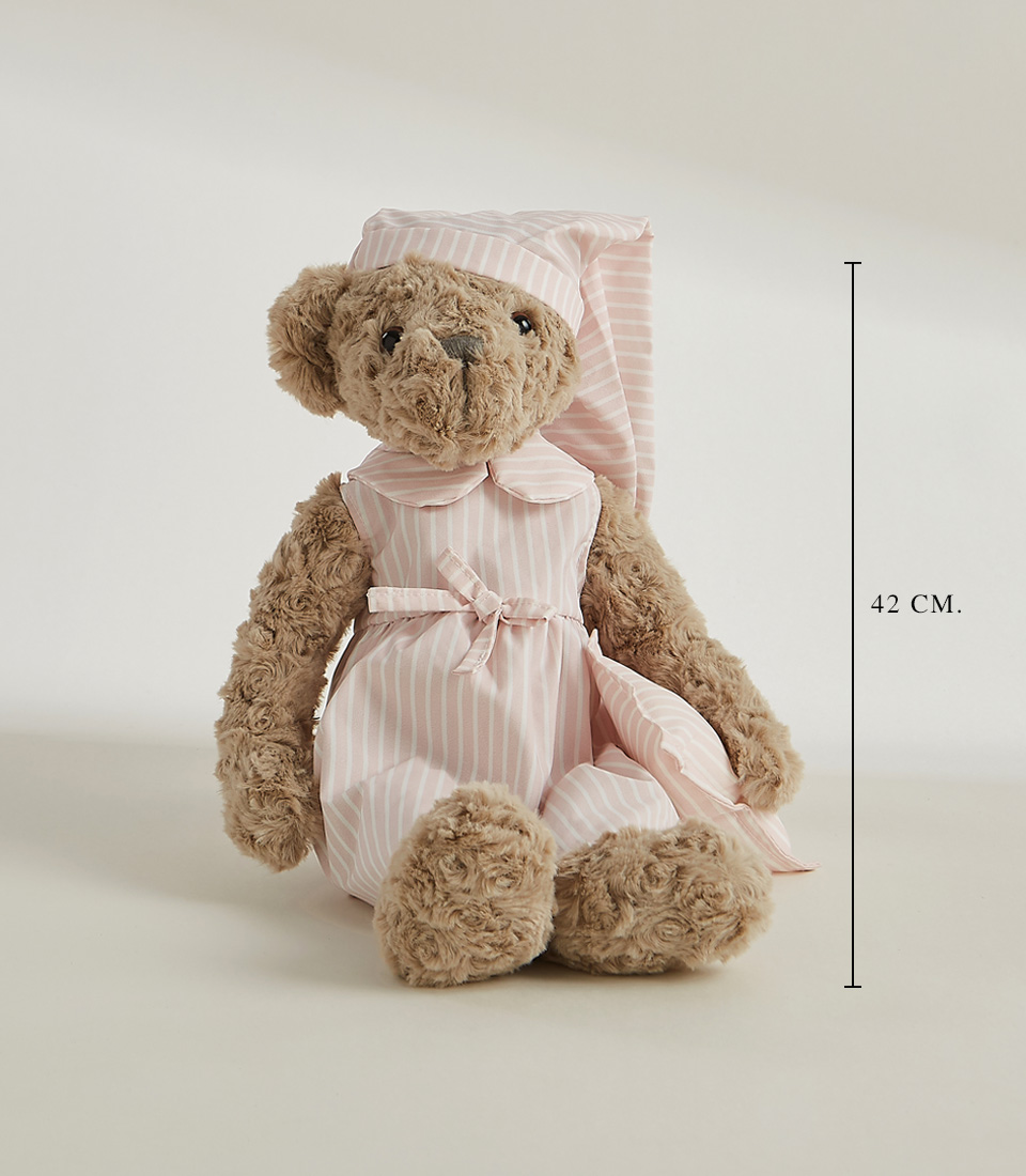 A fuzzy gray teddy bear in a white and pale pink striped dress and matching sleep cap stands upright on a plain white background, epitomizing the charm of soft toys.