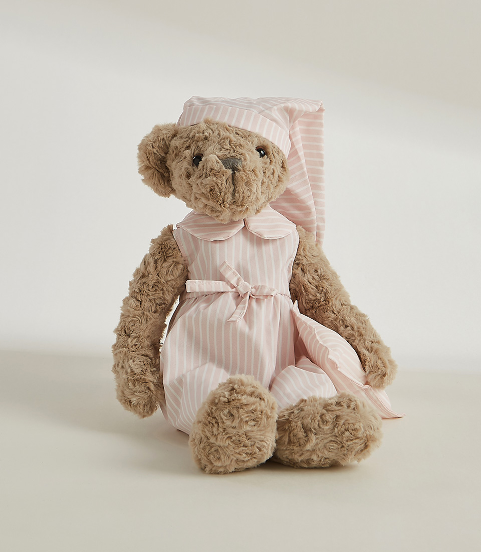 A fuzzy gray teddy bear in a white and pale pink striped dress and matching sleep cap stands upright on a plain white background, epitomizing the charm of soft toys.