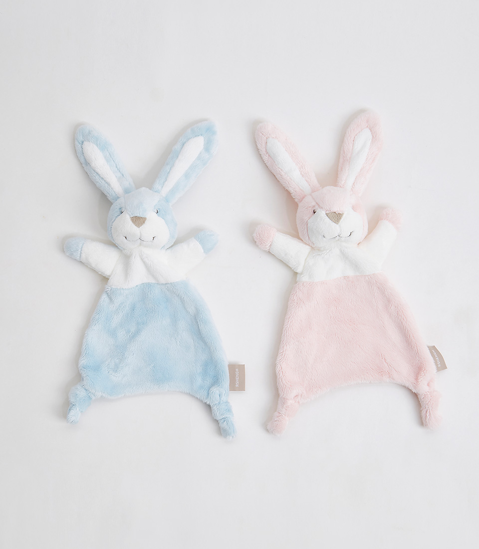 Two soft, plush bunny y saliva towels are laid flat on a white background. The left bunny, perfect for your baby, is light blue and white with a small tan tag, while the right cute bunny is light pink and white with a similar tag. Both bunnies have long ears, a smiling face, and knotted corners at the bottom.