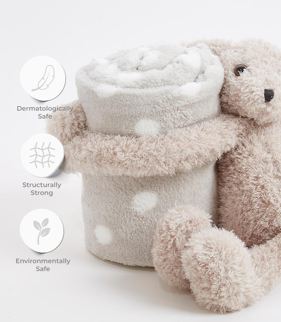 A cozy bunny plush cuddles a rolled-up gray blanket with white polka dots. Beside the blanket are icons with text: “Dermatologically Safe,” “Structurally Strong,” and “Environmentally Safe,” indicating the baby blanket's qualities.