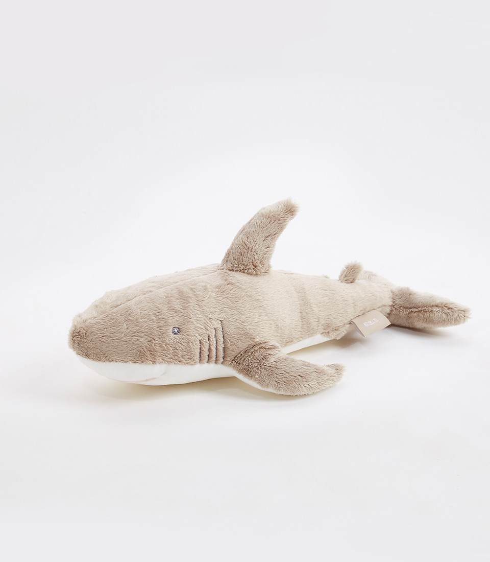 A soft, cuddly plush shark toy with light brown fur, small black eyes, a dorsal fin, pectoral fins, and a tail fin is lying on a white background. This adorable plush shark soft toy is perfect for children.