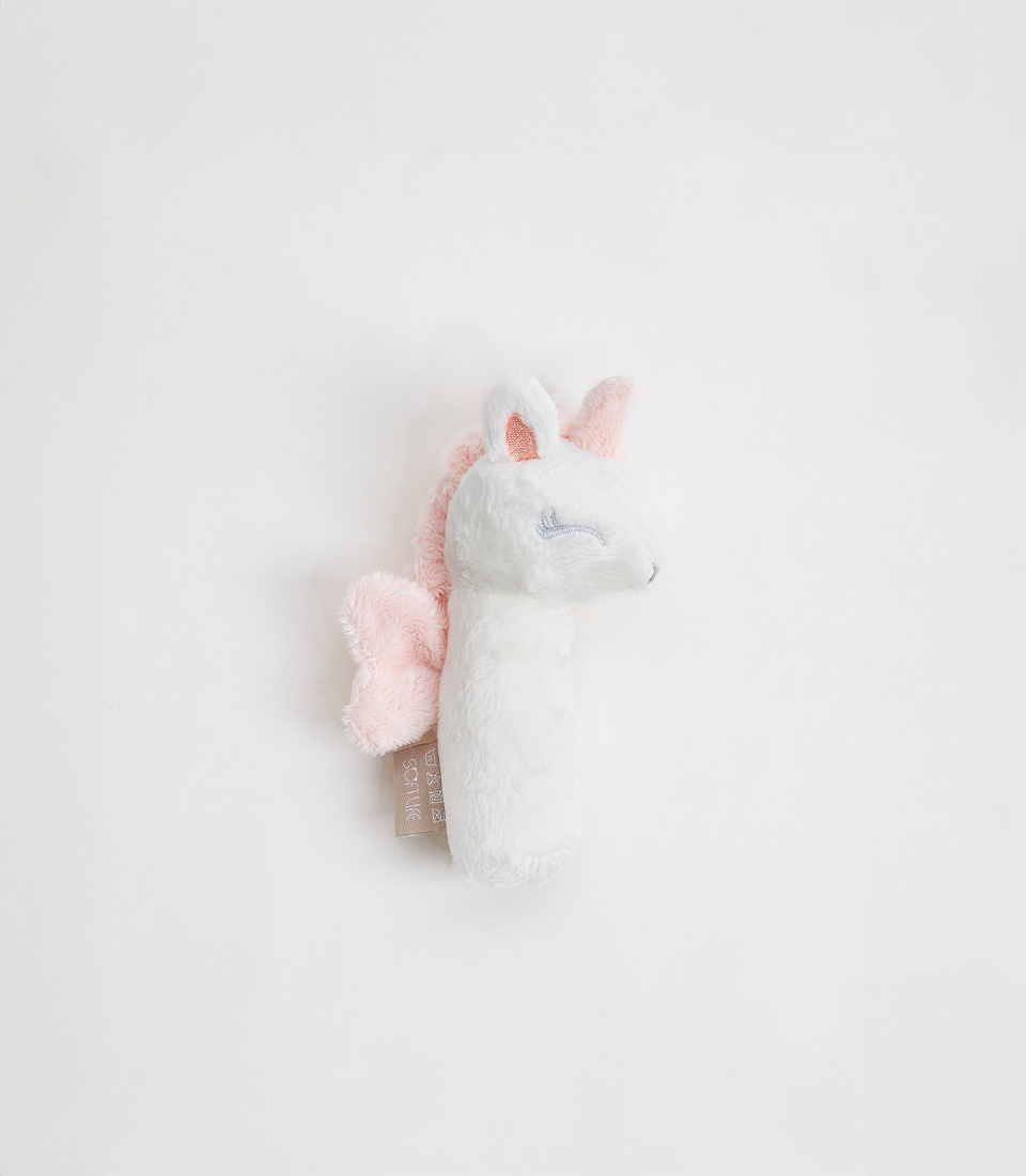 A soft unicorn plush toy bolster lies on a white background. The toy is predominantly white, with light pink fabric accents on its mane, ears, and wings. It has embroidered blue eyes that are closed, suggesting it is asleep or resting. A small tag is attached to its side.