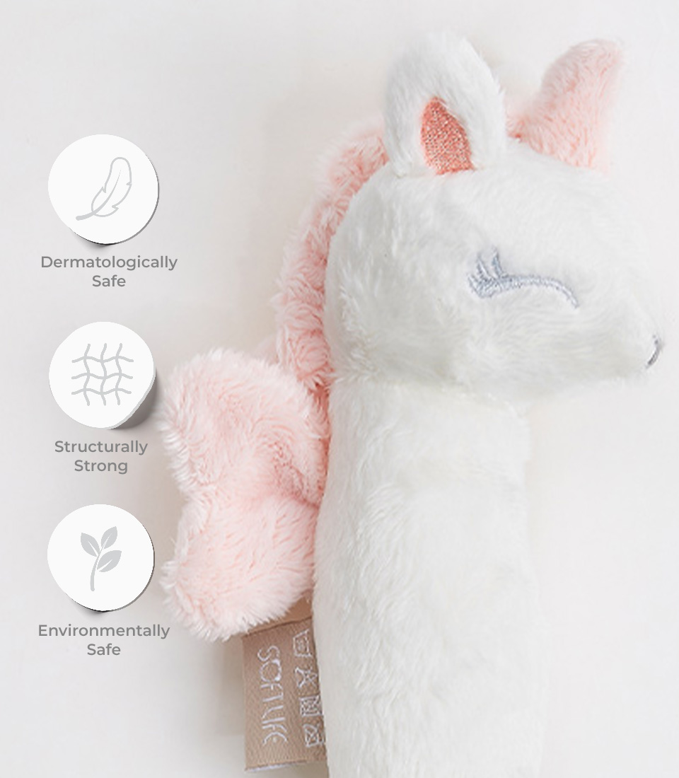 A soft unicorn plush toy bolster in white with pink accents is shown. The toy has closed eyes with embroidered lashes. Icons next to the toy indicate it is dermatologically safe, structurally strong, and environmentally safe. A sewn-in label reads 