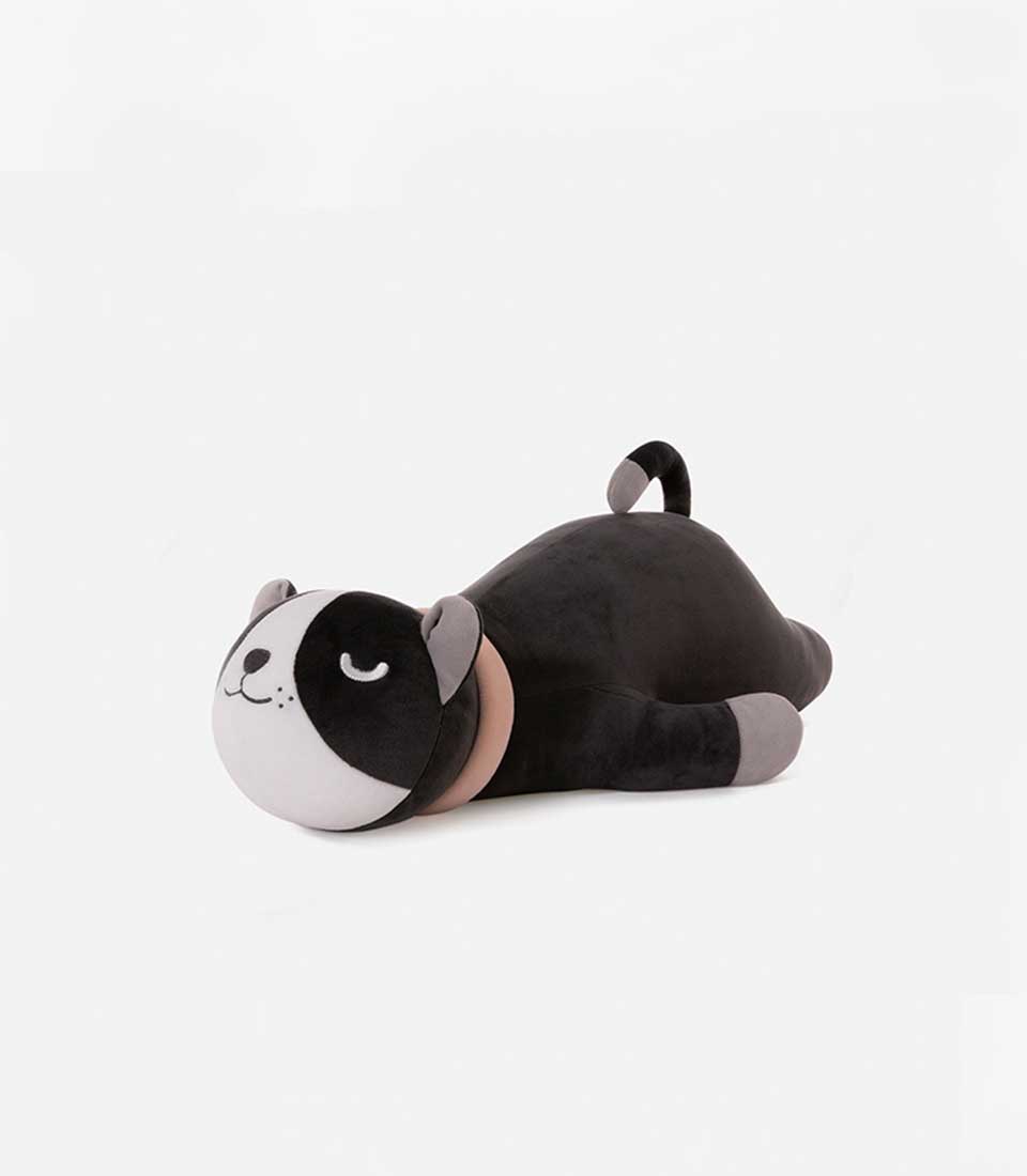 A black dog plush toy lying down with a grey muzzle, ears, and paws. The toy has a light pink collar and a small curled tail, featuring a happy, sleepy face with closed eyes, on a white background.