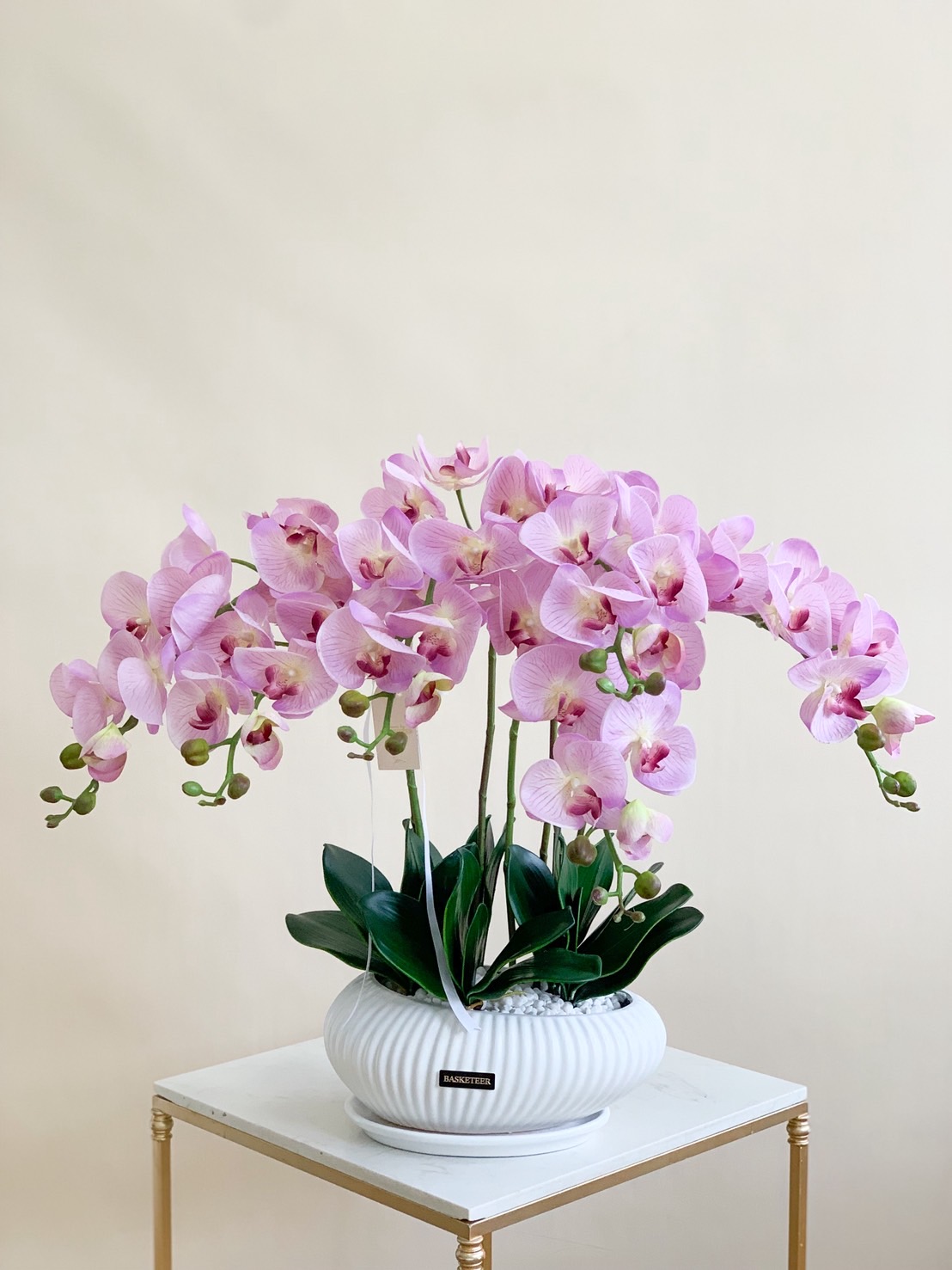 Beautiful pink orchid arrangement in a white ceramic vase with Basketeer branding, perfect for luxury gifts and decor.