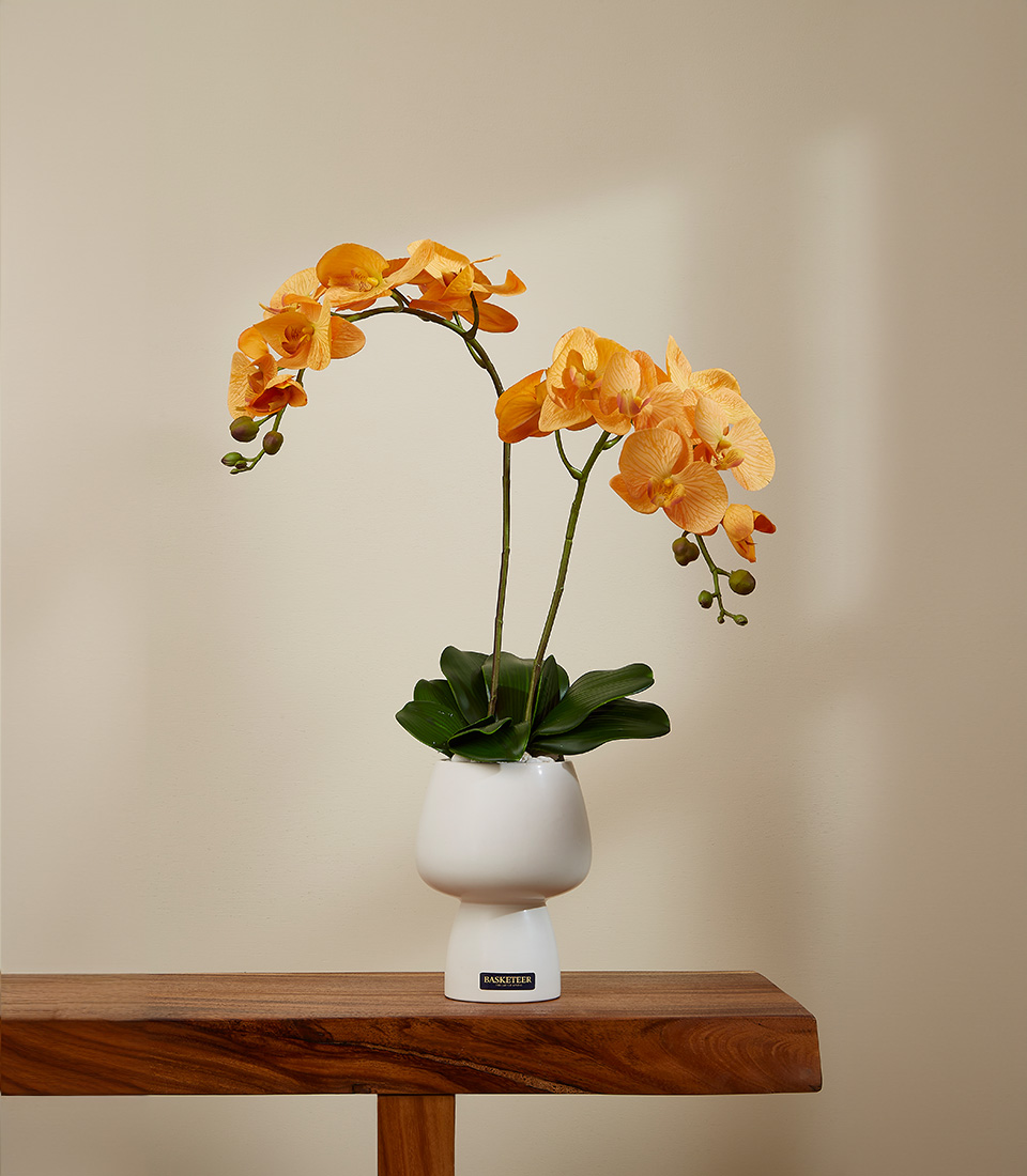 Lifelike golden-yellow Phalaenopsis orchid arrangement with realistic green stems and leaves in a modern white ceramic pot