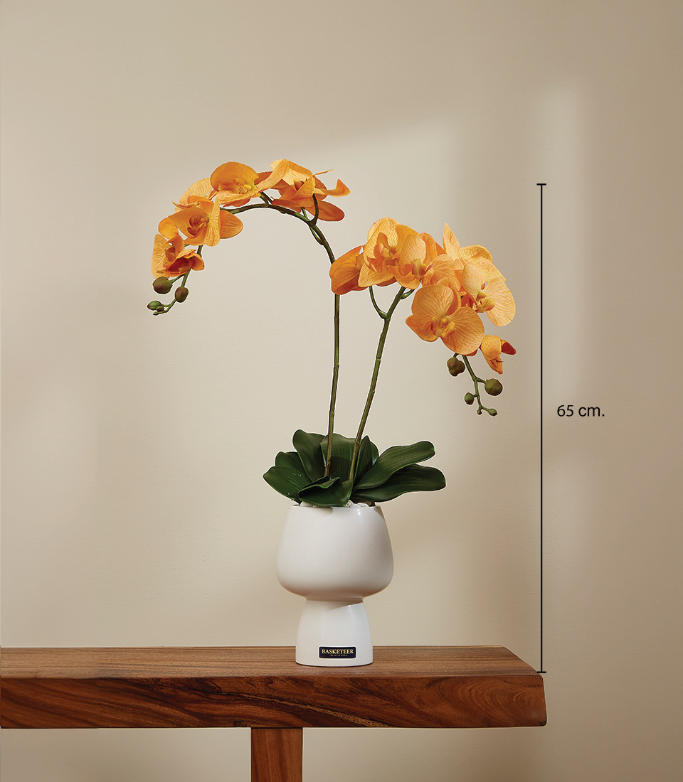 Lifelike golden-yellow Phalaenopsis orchid arrangement with realistic green stems and leaves in a modern white ceramic pot, measuring 65 cm in height