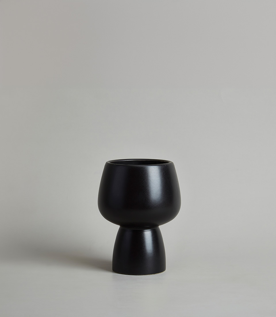 Modern black ceramic vase with unique silhouette featuring a rounded top and tapered base with a light gray background.