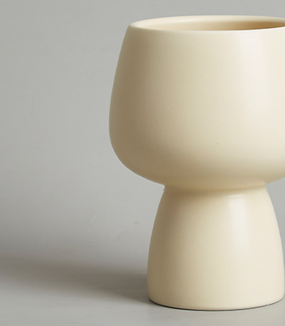 Close-up view of a modern beige ceramic vase with a minimalist design, featuring a rounded bowl-shaped top and a narrow bas