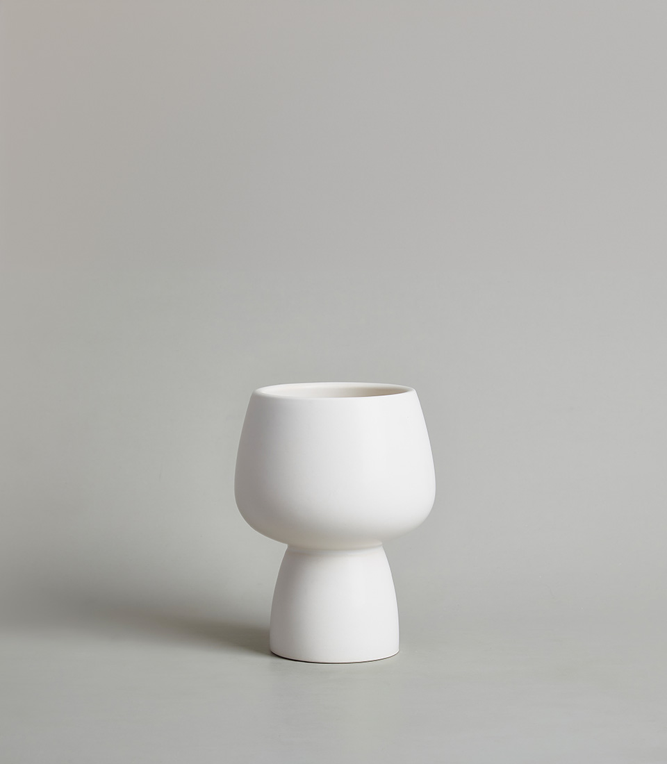 Modern white ceramic vase with a minimalist design, featuring a rounded bowl-shaped top and a narrow base, against a neutral background.