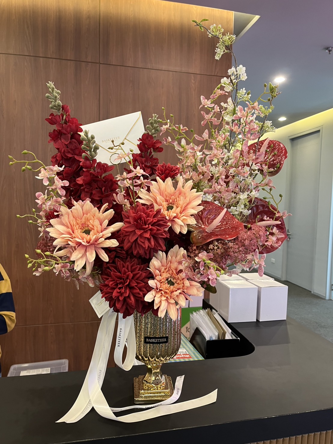 Luxury gold vase arrangement with deep red and peach dahlias, orchids, and anthuriums, accented with pink blooms.