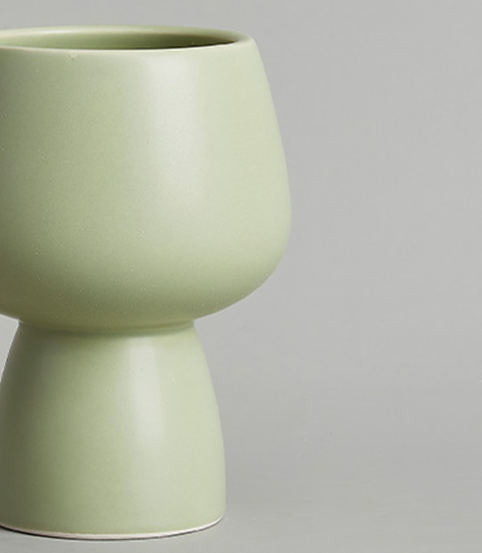 Close-up of a modern light green ceramic vase with a minimalist design, featuring a rounded bowl-shaped top and a narrow base, against a neutral background.