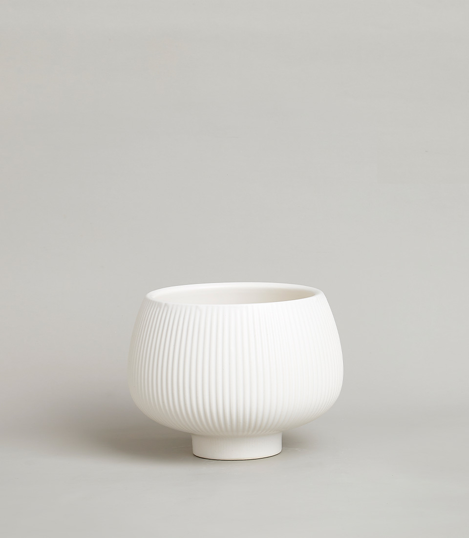 White ribbed ceramic bowl vase with a modern design against a neutral background.