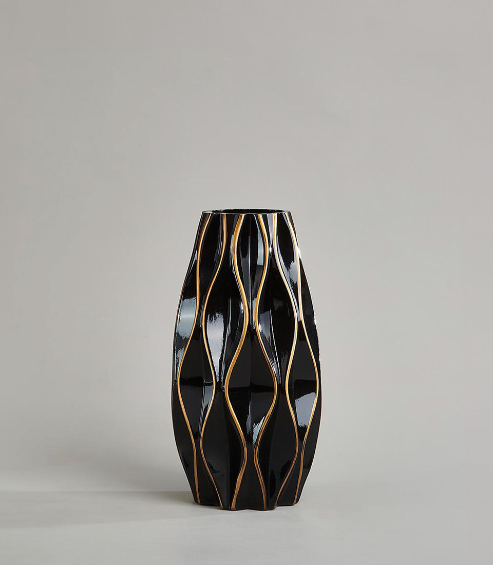 Black ceramic vase with gold accents and a wavy design against a neutral background.