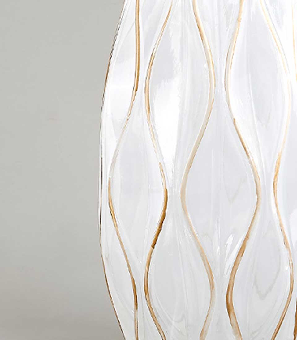 Close-up of White ceramic vase with gold accents and wavy design.