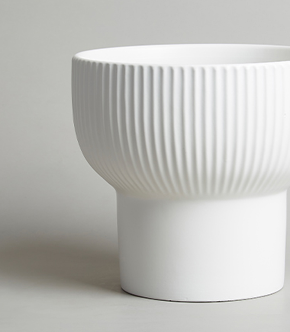 Close-up of Modern White Ceramic Vase with Ribbed Design on a Grey Background.