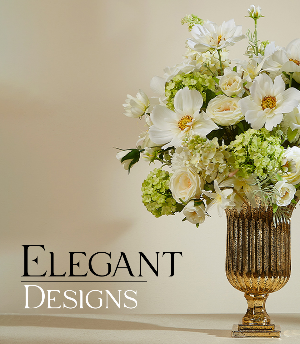 Elegant Designs artificial flower arrangement featuring lifelike white roses, daisies, and green hydrangeas in a luxurious gold vase on a beige table.