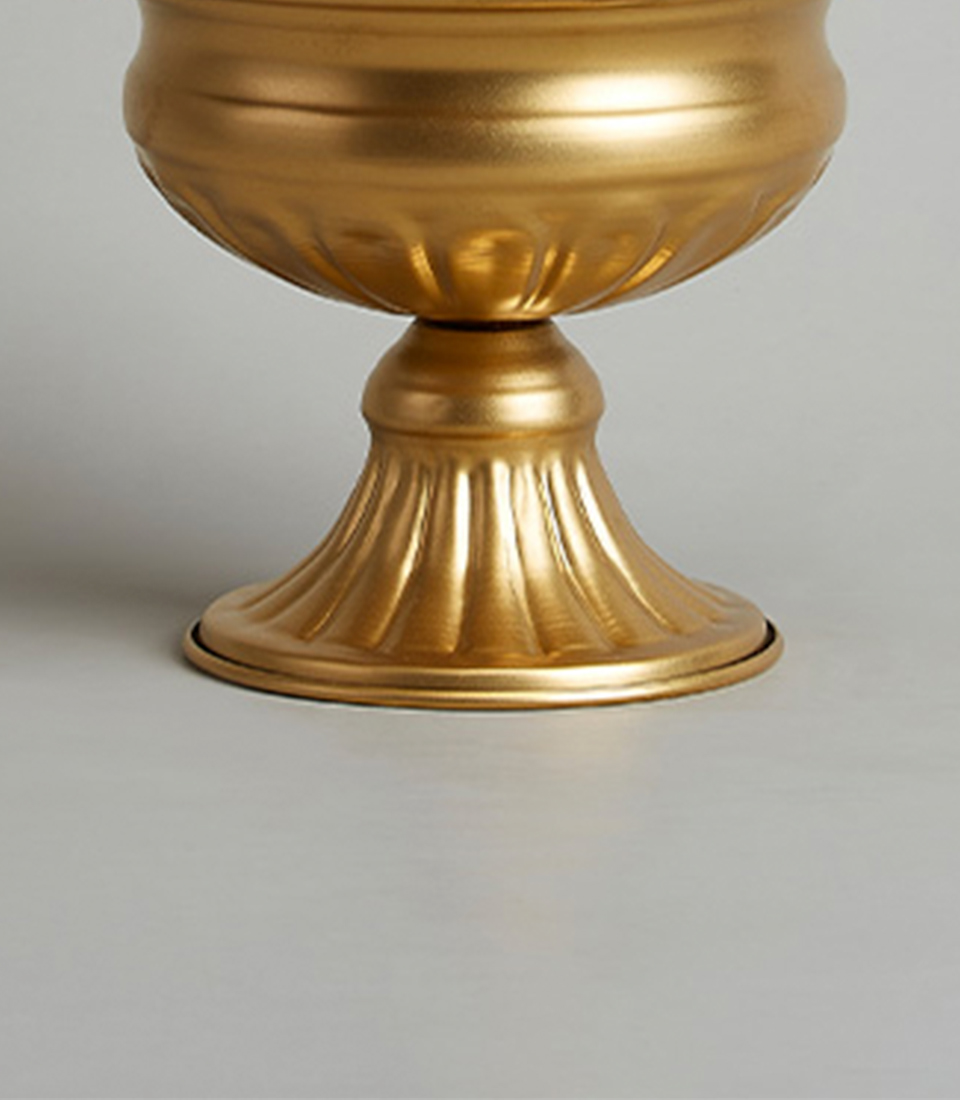 Close-up of the base of a gold steel pedestal vase with a fluted design.