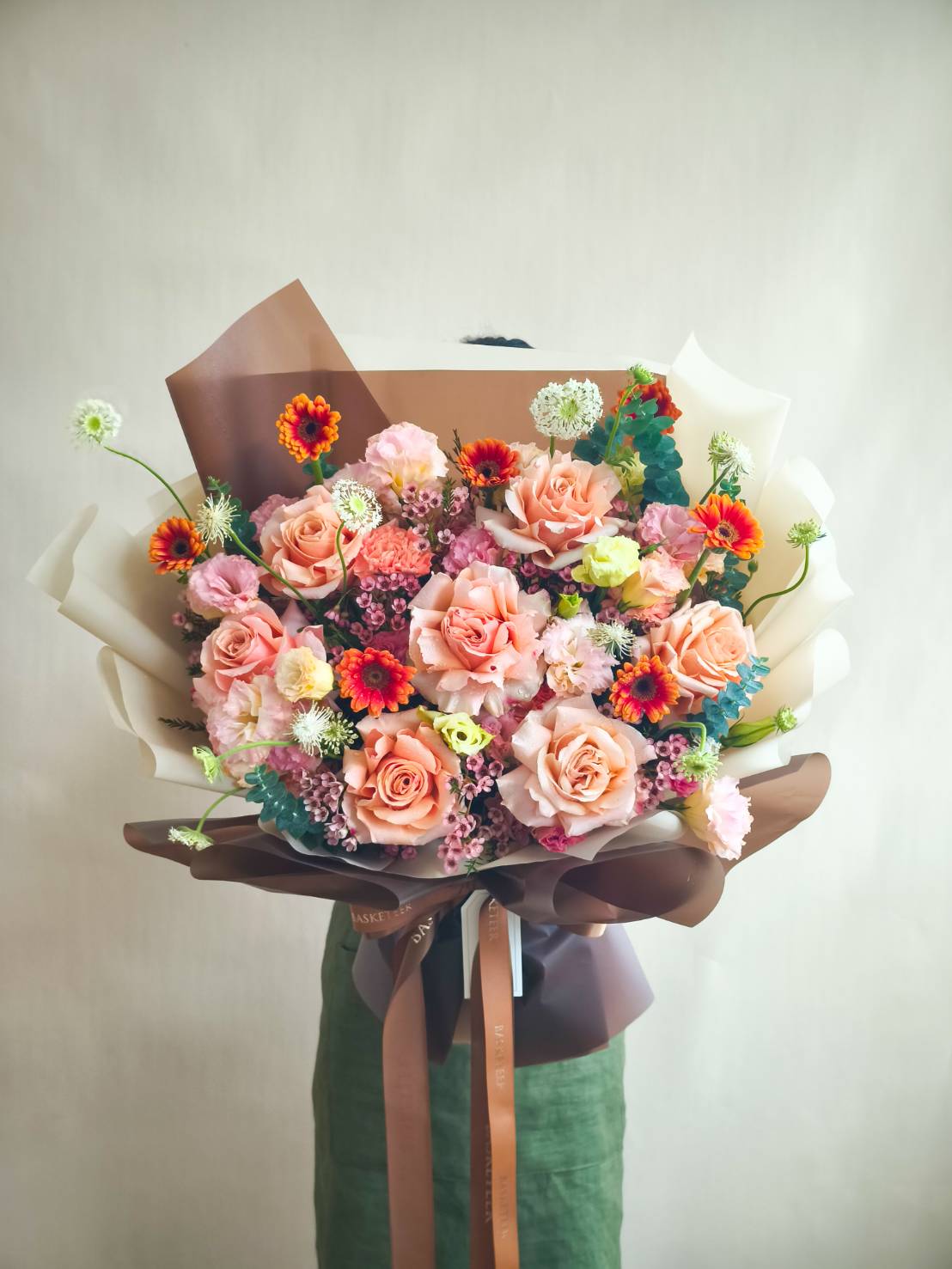 Luxury bouquet of peach and pink roses with vibrant mixed flowers, wrapped in elegant brown and cream paper.