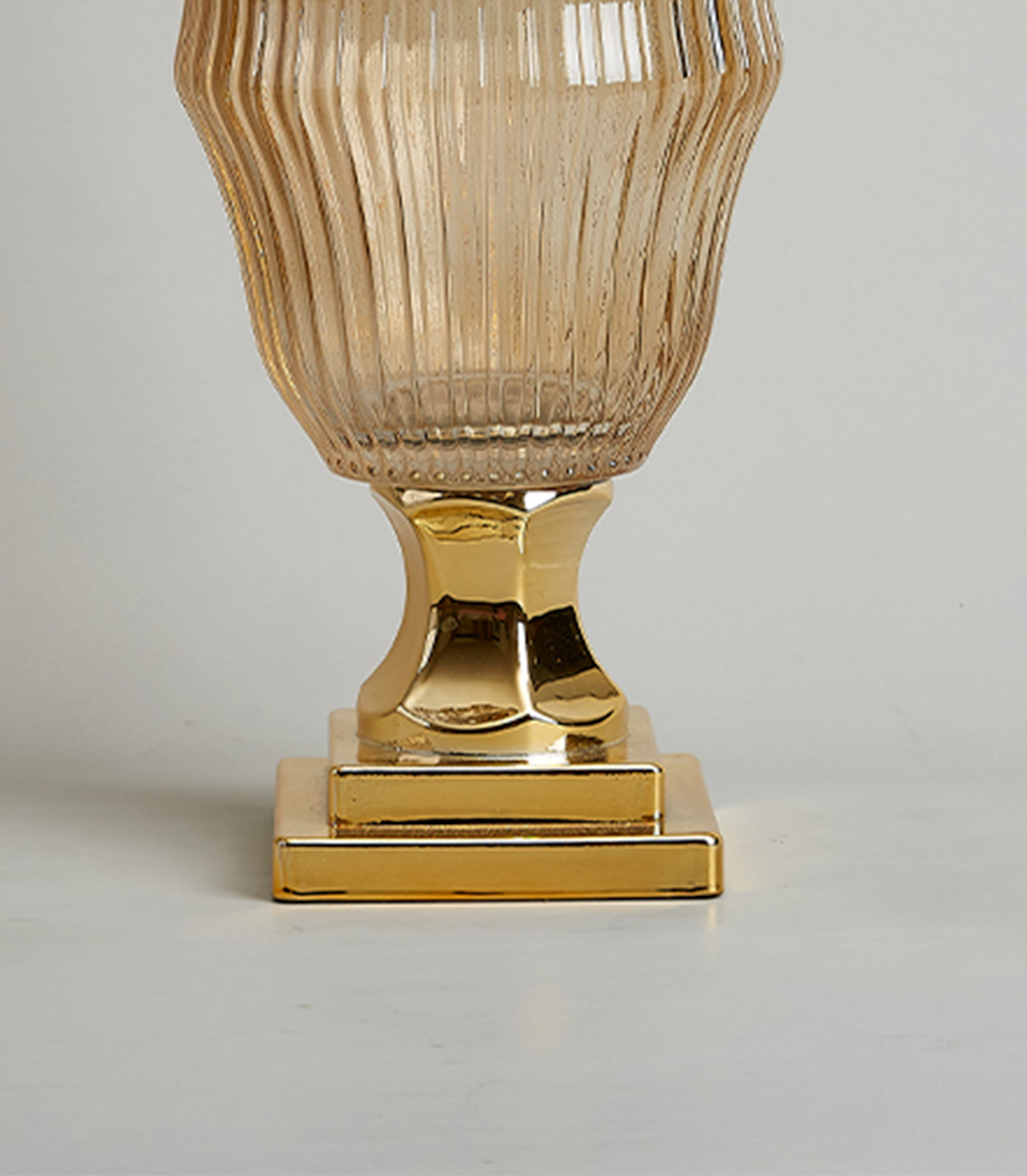 Close-up of Elegant amber glass vase with a ribbed texture and gold base on a white background.
