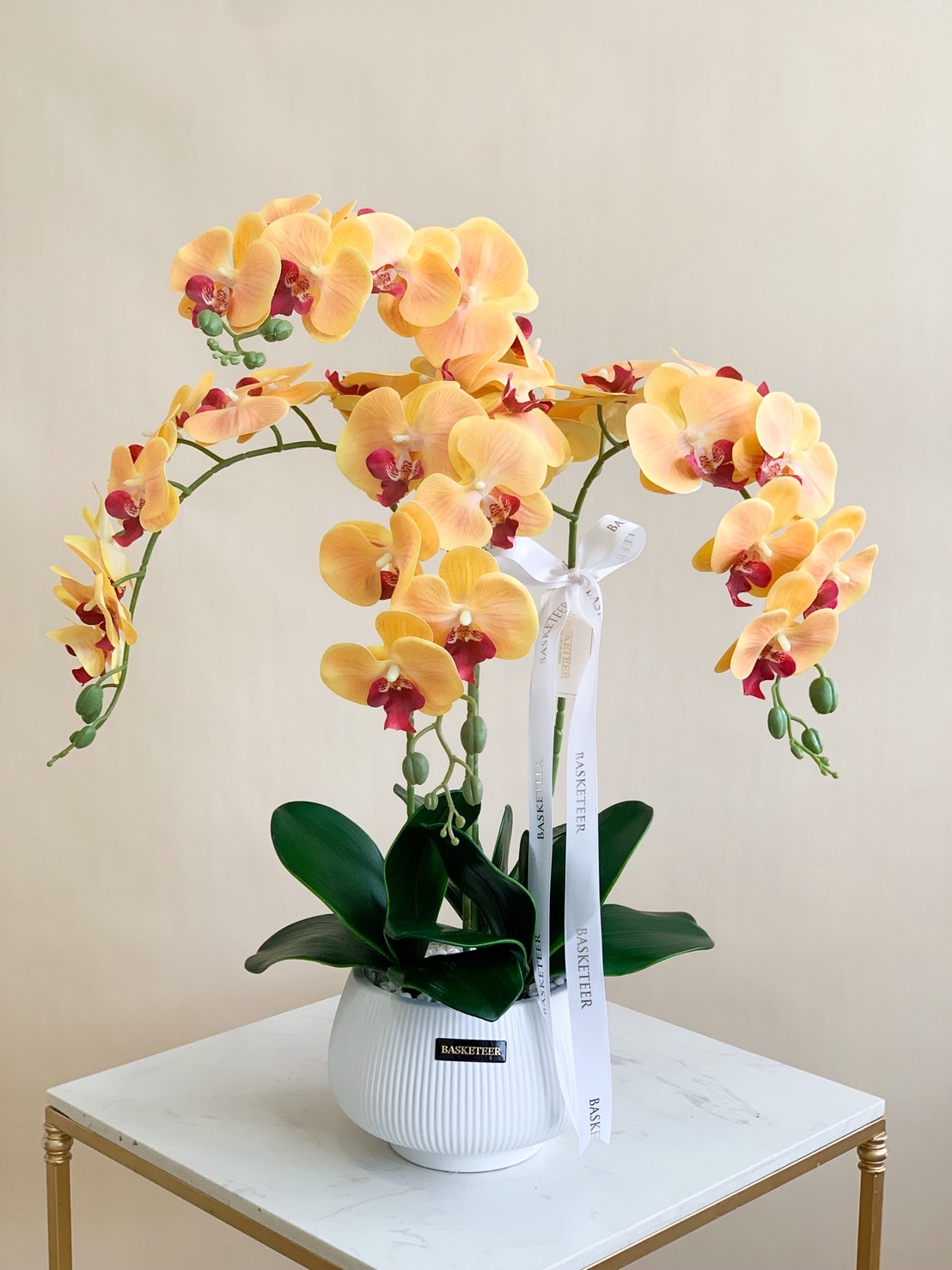 Golden yellow phalaenopsis orchid with orange-red centres in a white ceramic vase for premium gifting.