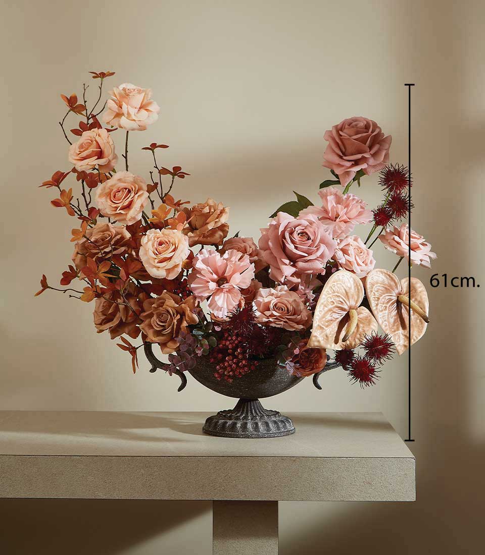 Artificial flower arrangement in decorative vase with pink, brown and peach flowers on a beige table and against a beige background, featuring a height measurement of 61 cm.