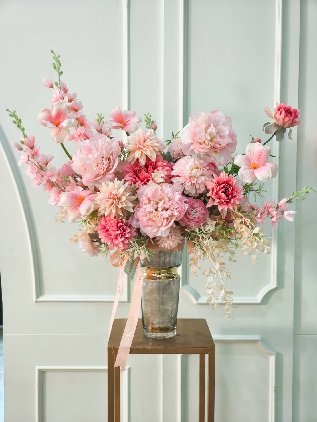Luxury tall glass vase with pink peonies, dahlias, lisianthus, and pastel blooms, accented with lush greenery and peach ribbons.