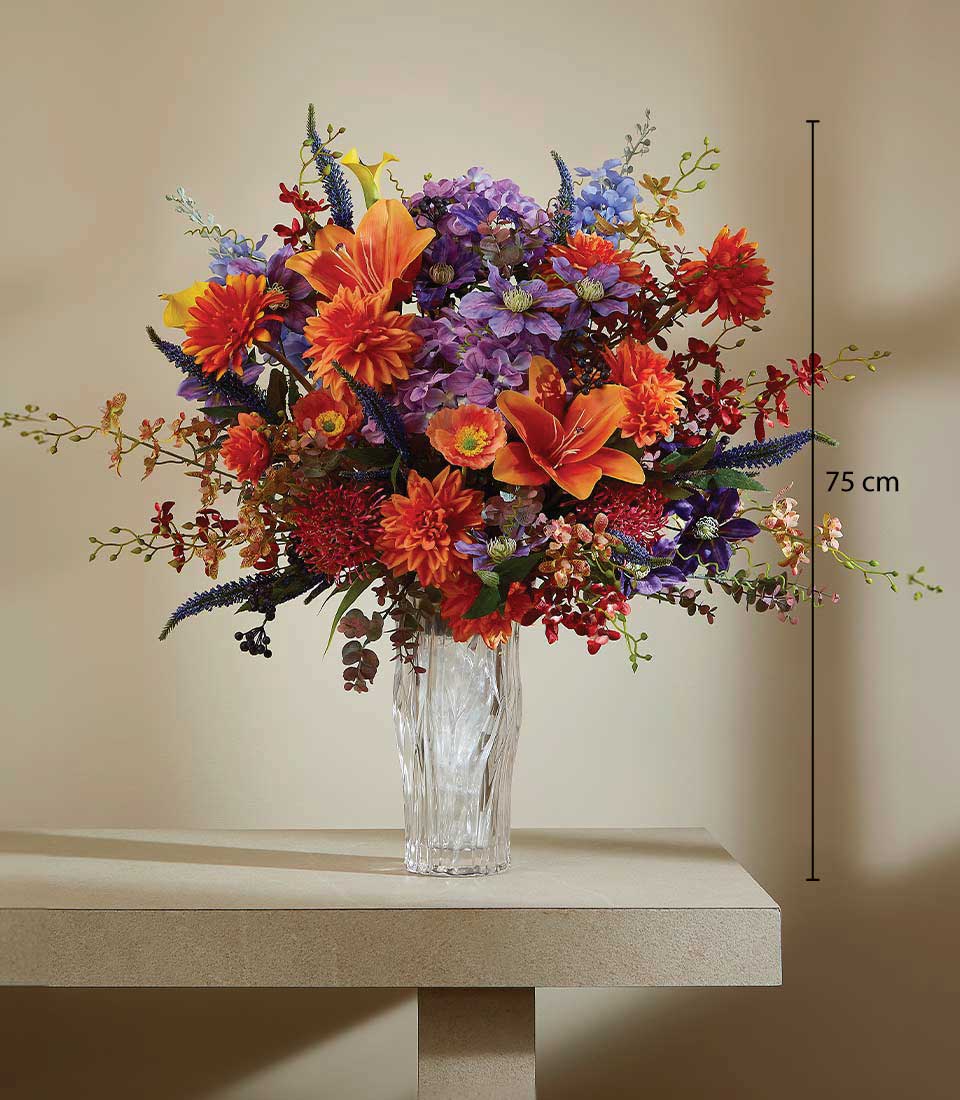 Vibrant artificial flower arrangement in a clear textured vase on a beige table and against a beige background, featuring a height measurement of 75 cm.