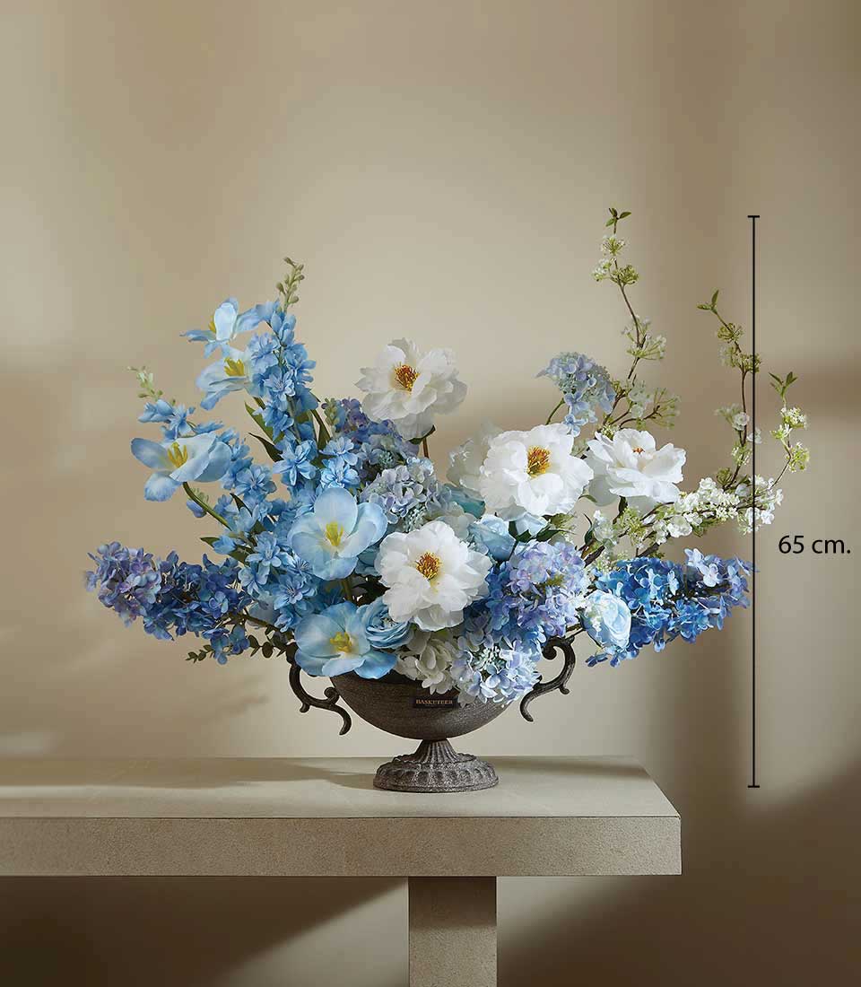 Artificial blue and white floral arrangement in an ornate pedestal vase on a beige table, displayed on a beige background, featuring a height measurement of 65 cm.