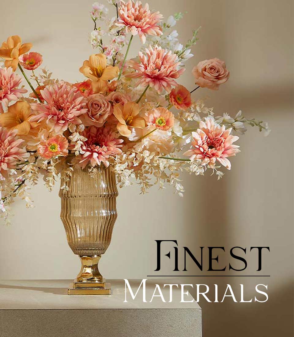 Artificial flower arrangement with soft peach dahlias, creamy orchids, and delicate roses in a tall gold vase on a table, displayed on a beige background with text 