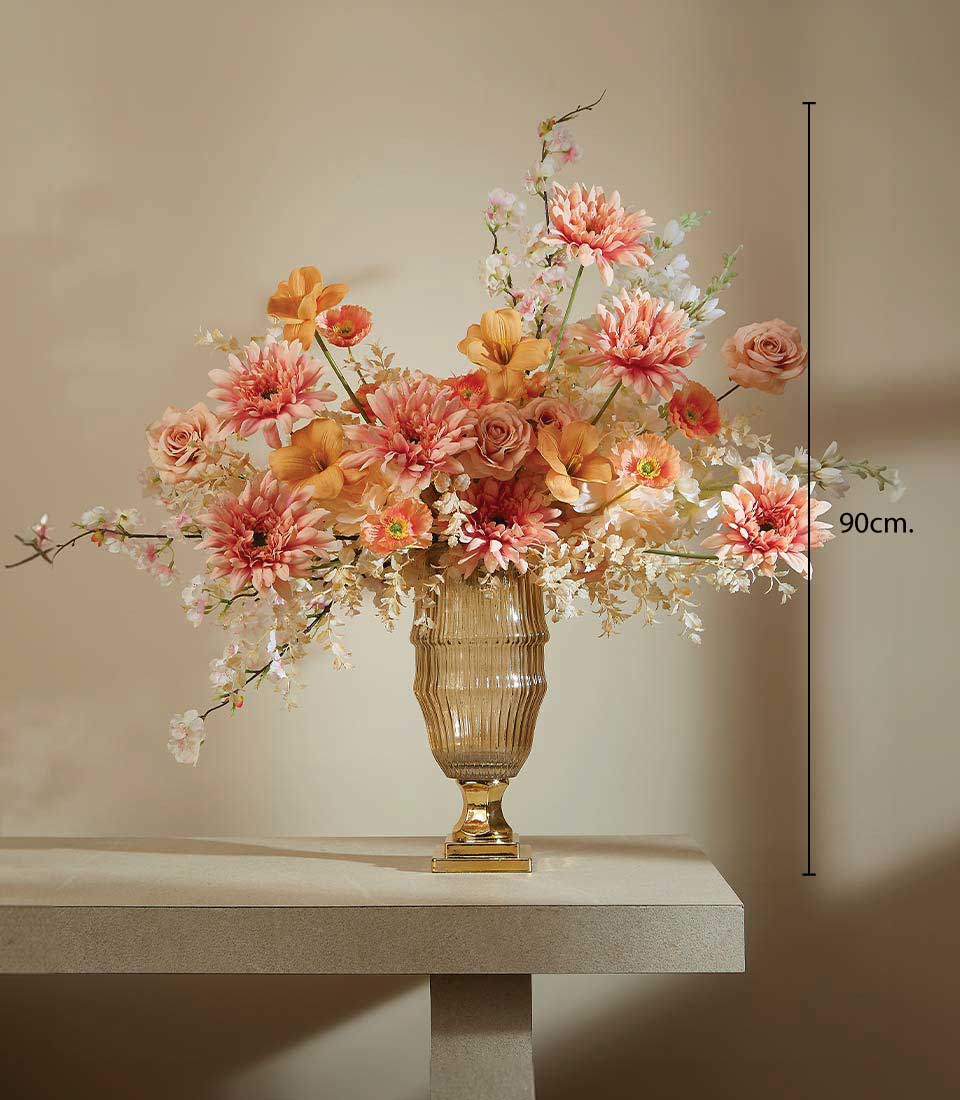 Artificial flower arrangement with soft peach dahlias, creamy orchids, and delicate roses in a tall gold vase on a table, displayed on a beige background, featuring a height measurement of 90 cm.