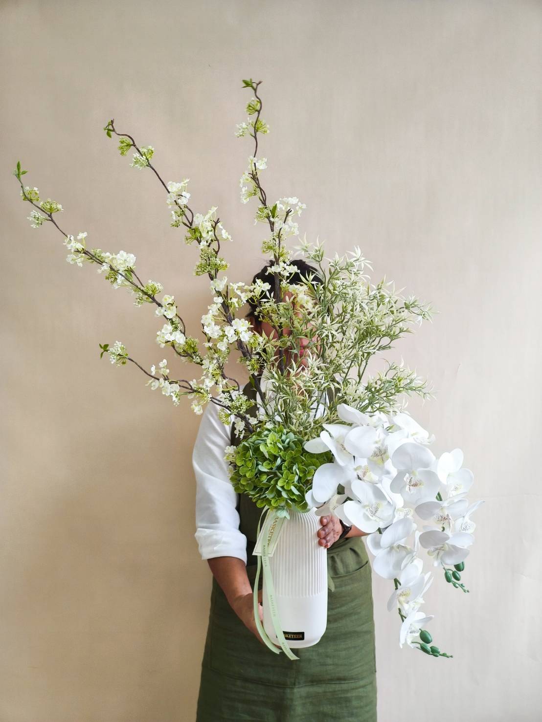 Tall white vase with cascading white orchids, cherry blossom branches, green hydrangeas, and foliage.
