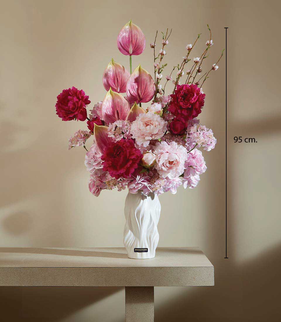 Artificial flower arrangement in a white wave-design vase, featuring vibrant pink and deep burgundy blossoms on a table, displayed on a beige background, featuring a height measurement of 95 cm.