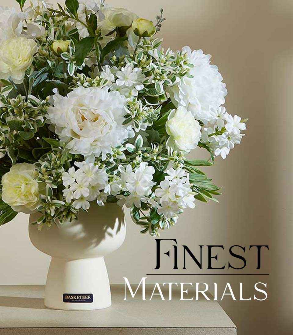 Artificial white flower arrangement with green foliage in a modern white ceramic vase on a table with text 