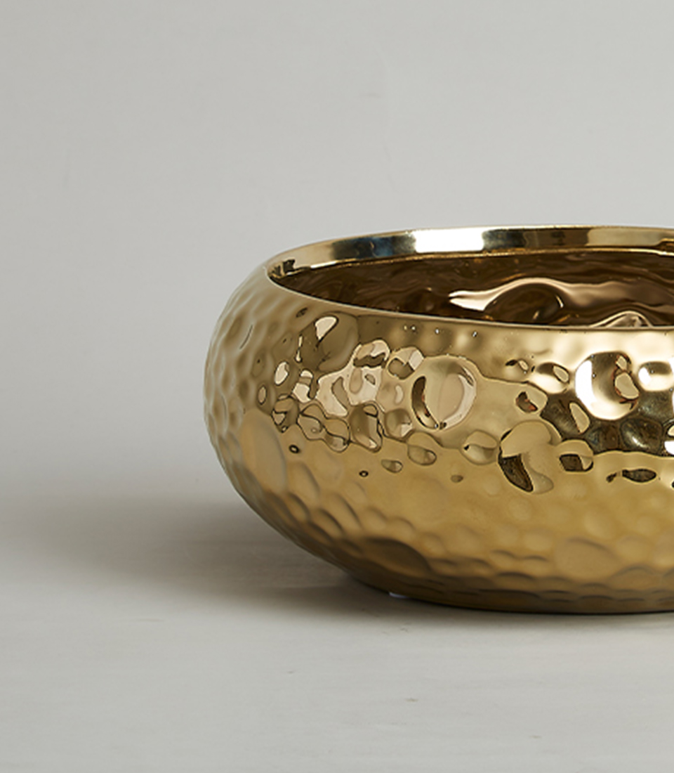 Close-up of gold hammered ceramic bowl, showing textured and reflective surface.