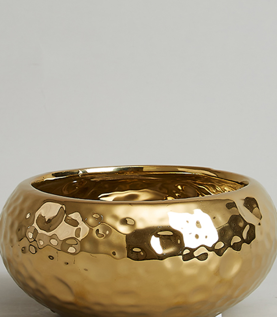 Close-up of gold hammered ceramic bowl, showing textured and reflective surface.
