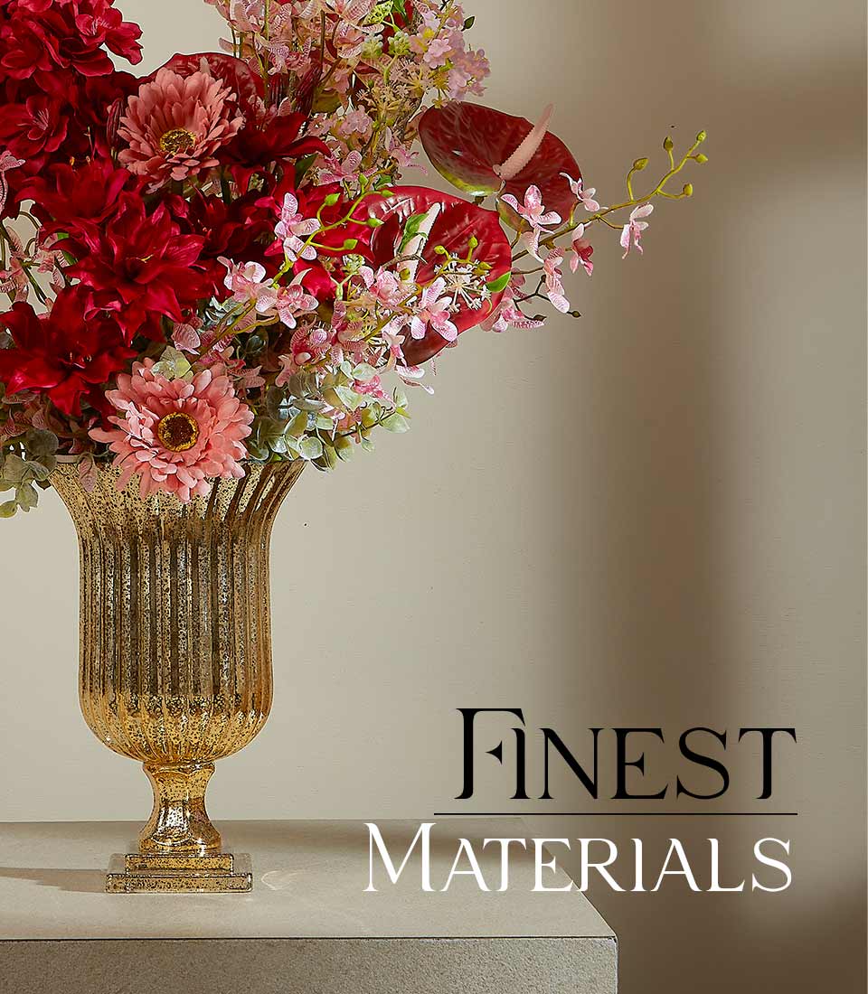 Close-up of elegant red and pink artificial flower arrangement in a tall, fluted gold vase with a 