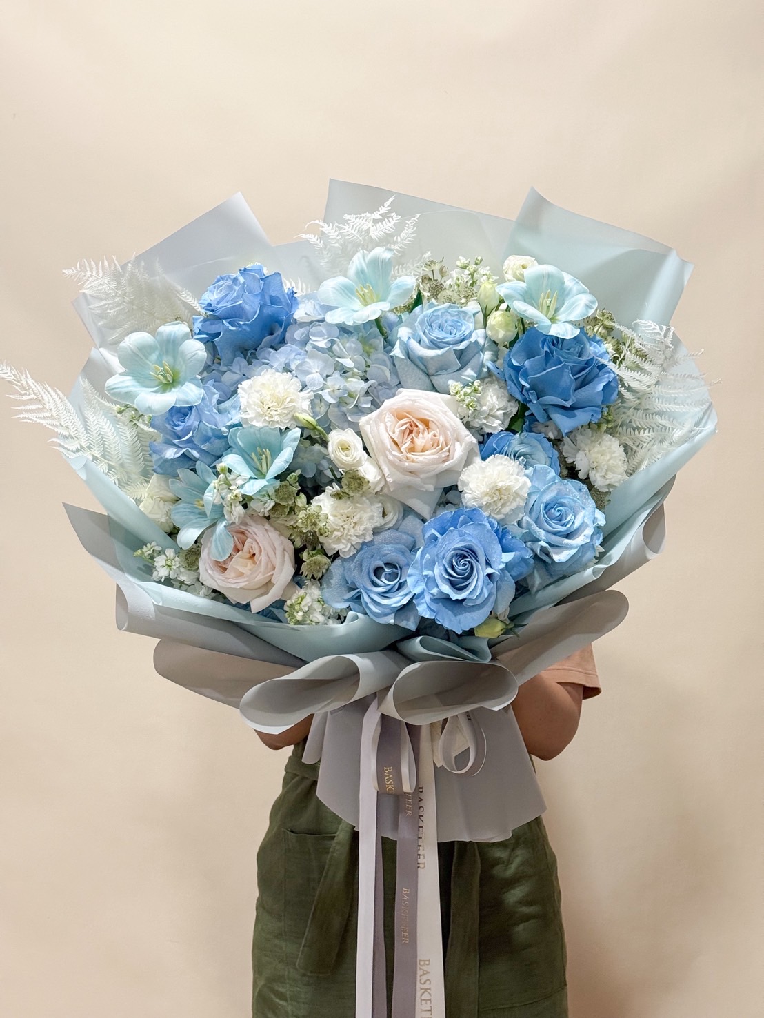 Large bouquet of blue and white roses with soft cream roses, hydrangeas, carnations, and delicate fillers, wrapped in pastel blue paper.