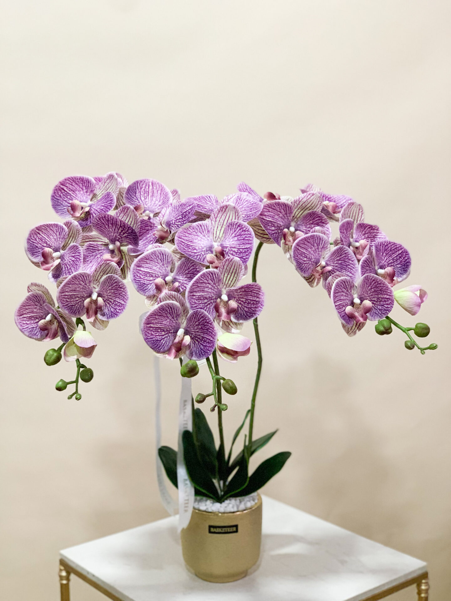 A radiant pink orchid arrangement set in a sleek gold pot. The vibrant pink blossoms, detailed with realistic petals and lush green leaves, stand out against the neutral background, making this 70 cm tall arrangement a sophisticated addition to any interior space.