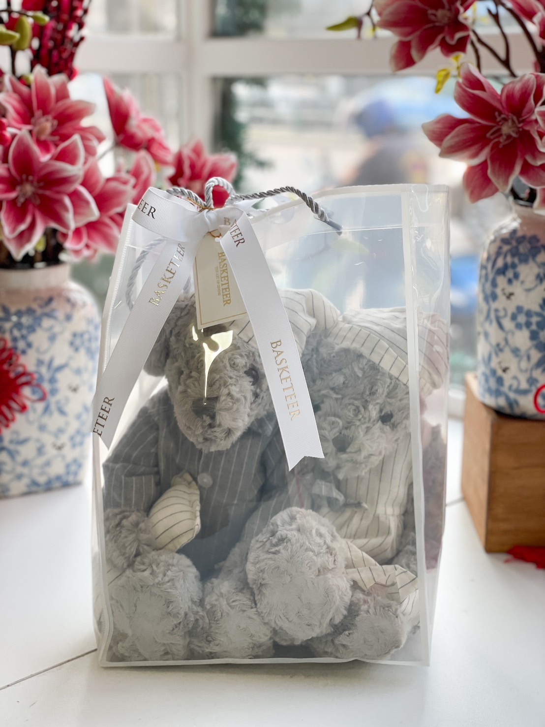 Luxury grey teddy bear in a striped suit, elegantly presented in a transparent gift bag with a white Basketeer ribbon.