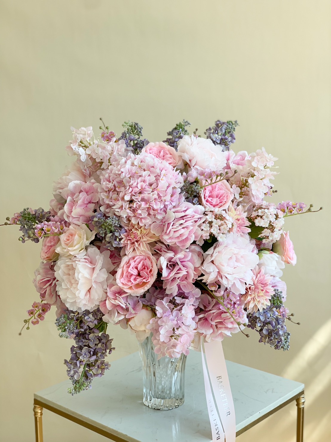 Elegant pink and lavender floral arrangement in a crystal vase with hydrangeas, roses, and peonies.