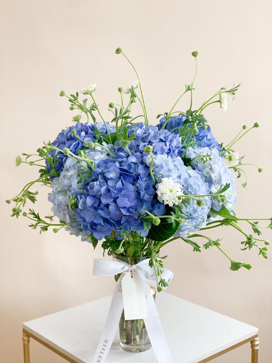 stunning bouquet featuring a mix of pastel-colored hydrangeas in shades of blue and white, complemented by delicate green foliage and wrapped in soft paper